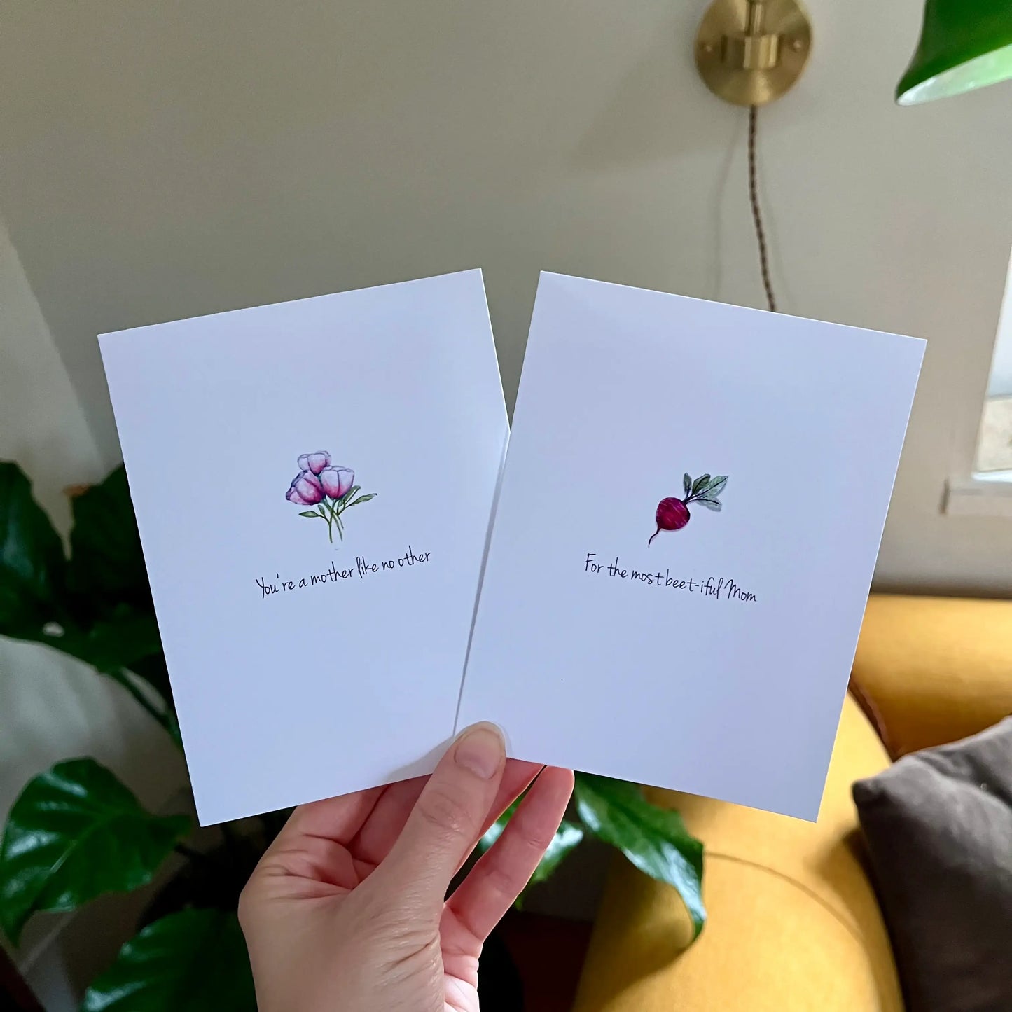 Hand holding two handcrafted greeting cards with floral art and Mother's Day messages